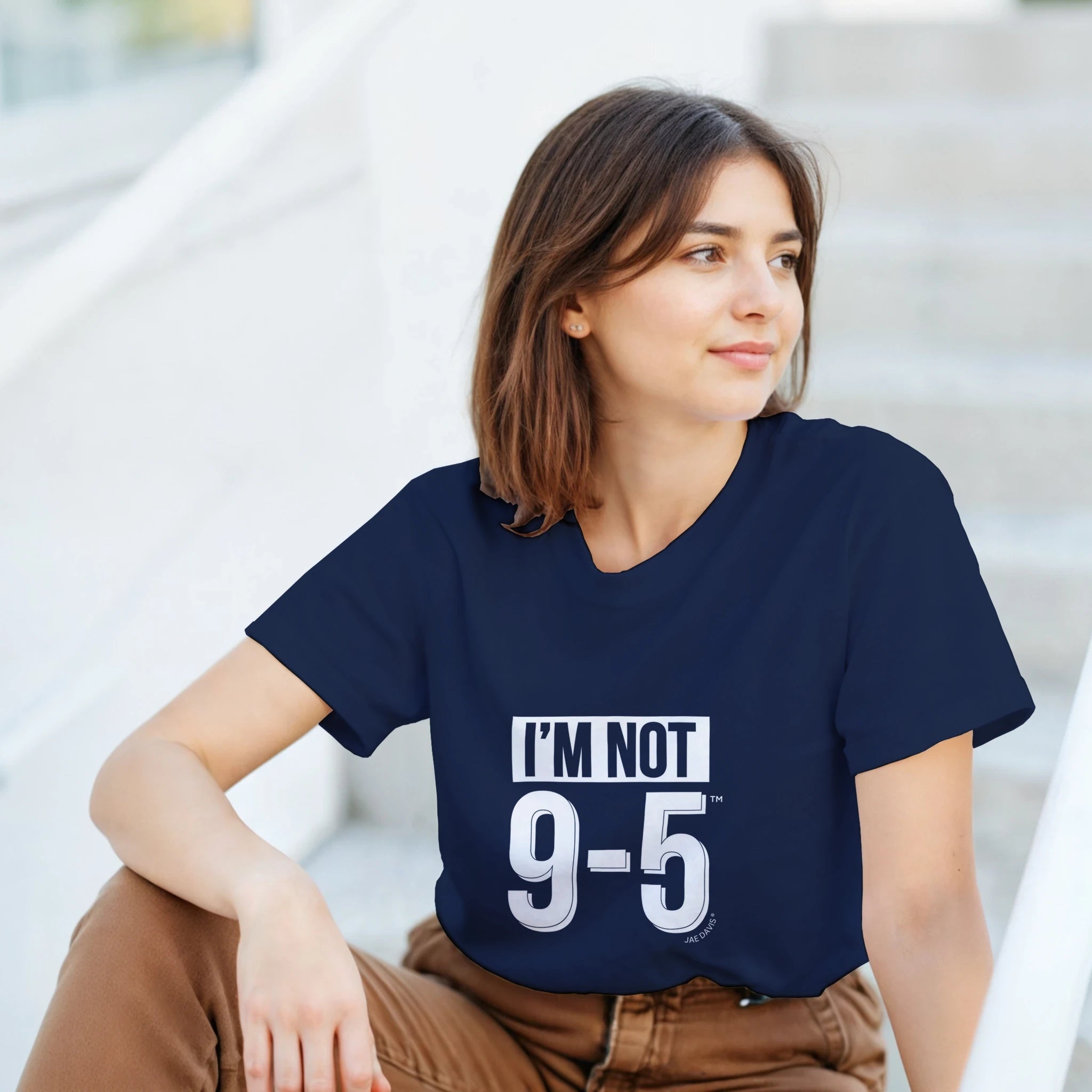 Woman wearing a navy blue t-shirt with 'I'M NOT 9-5' text, sitting outdoors.