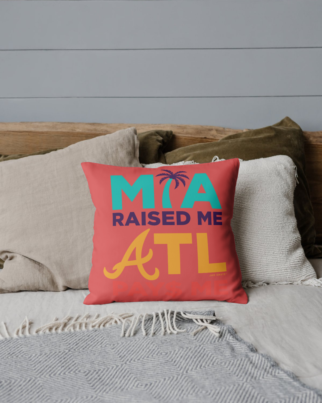 Red pillow with 'MIA Raised Me ATL' text on a couch with neutral pillows and a gray wall background