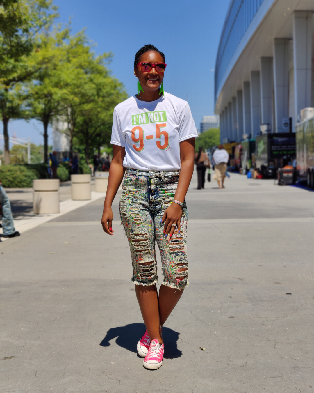 Person wearing a white t-shirt with text and colorful pants standing outdoors.