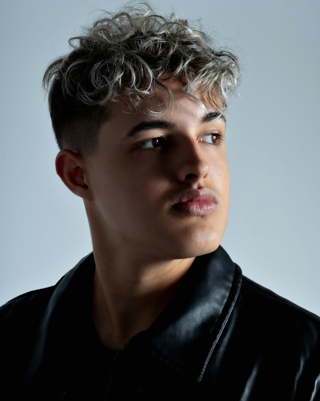 Man with styled hair wearing a black leather jacket against a gray background