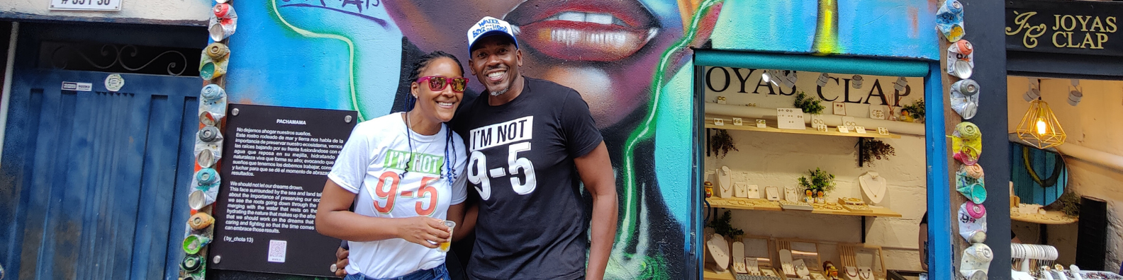 Two people standing in front of a colorful mural with a store entrance in the background.