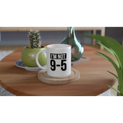 White mug with 'I'm not 9-5' text on a wooden table with plants